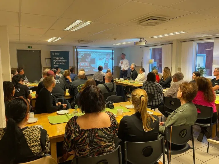 Personer samlade vid bord i ett konferensrum under en presentation